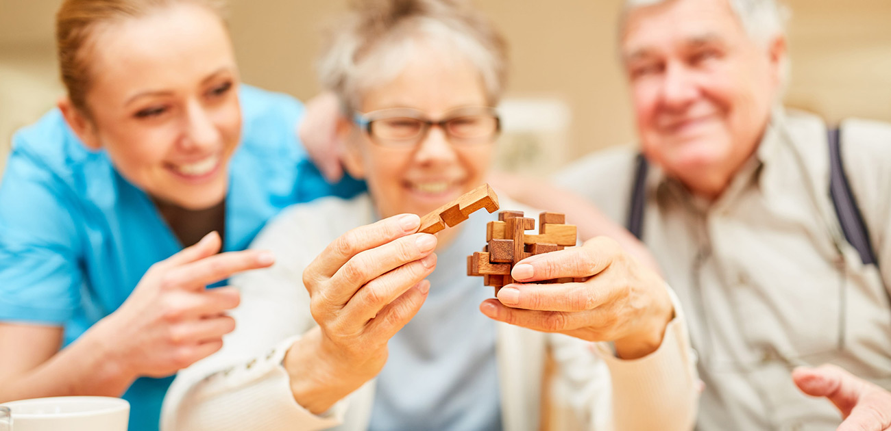 Demenz-bausteine Senioren setzen gemeinsam ein hölzernes Puzzle zusammen, begleitet von einer Pflegekraft.